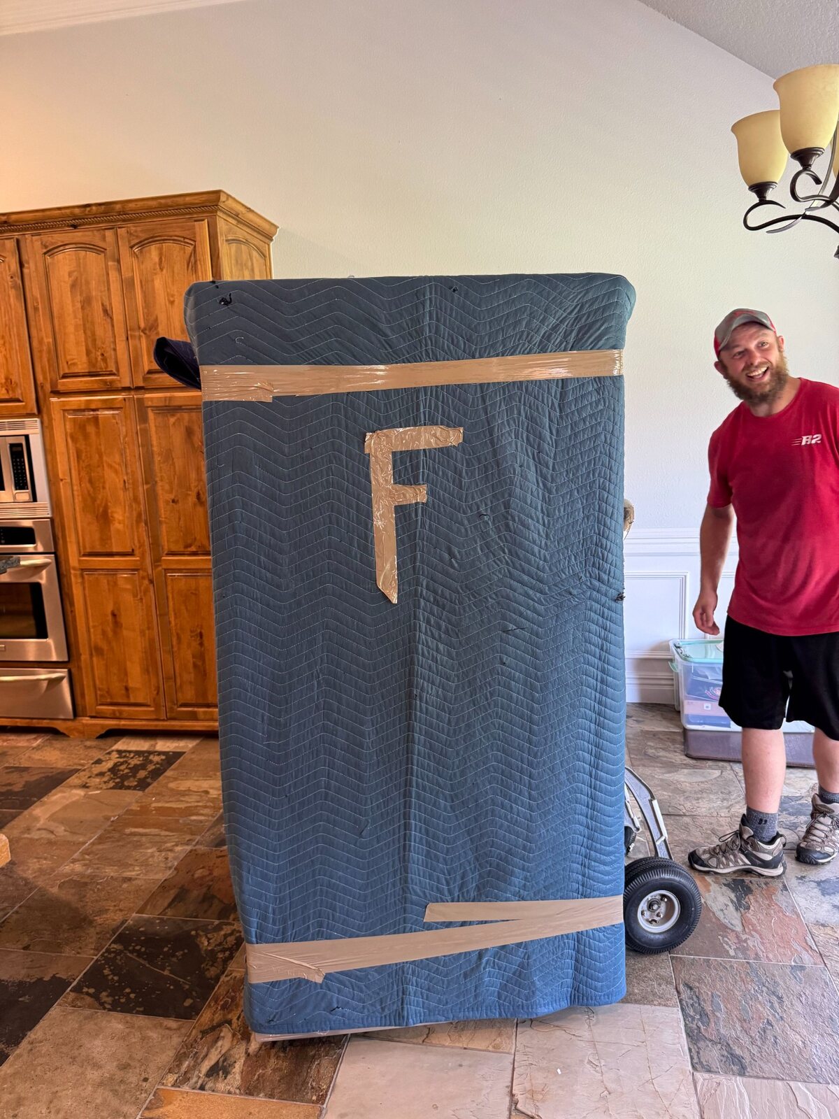 B2 mover Joe beside a padded furniture piece with a front-facing label during a Centerton move