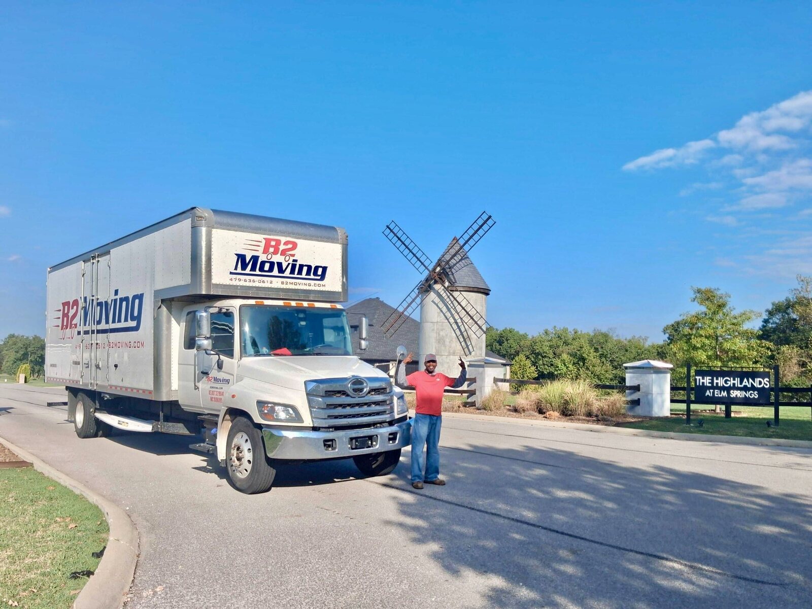B2 Moving teammate smiling beside a branded B2 truck and the windmill at The Highlands at Elm Springs