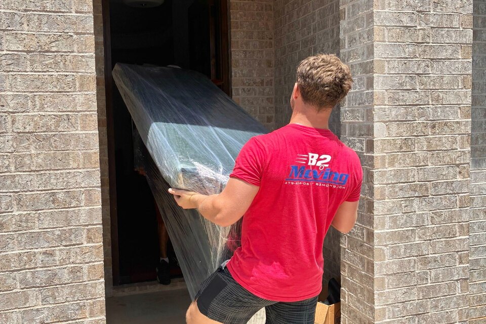 Kaden McCrary carrying a wrapped furniture piece through a residential doorway