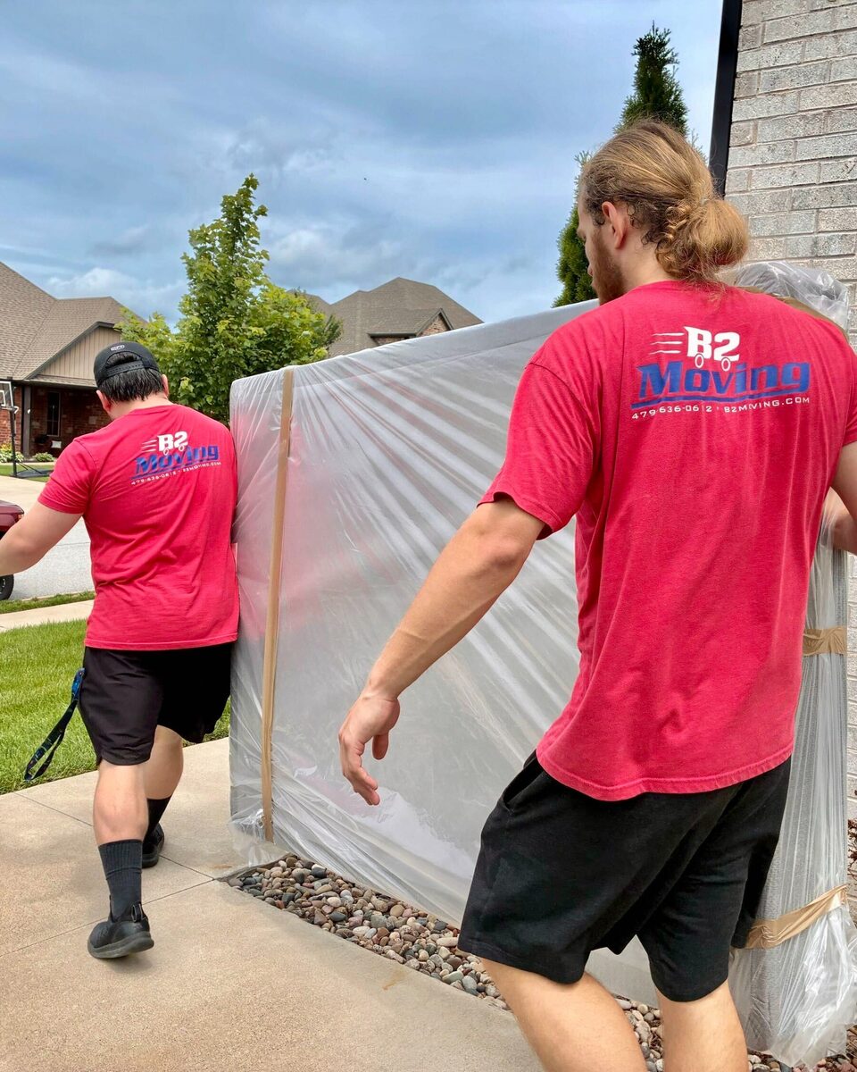 Isaac and Traven carrying a mattress sealed inside a protection bag