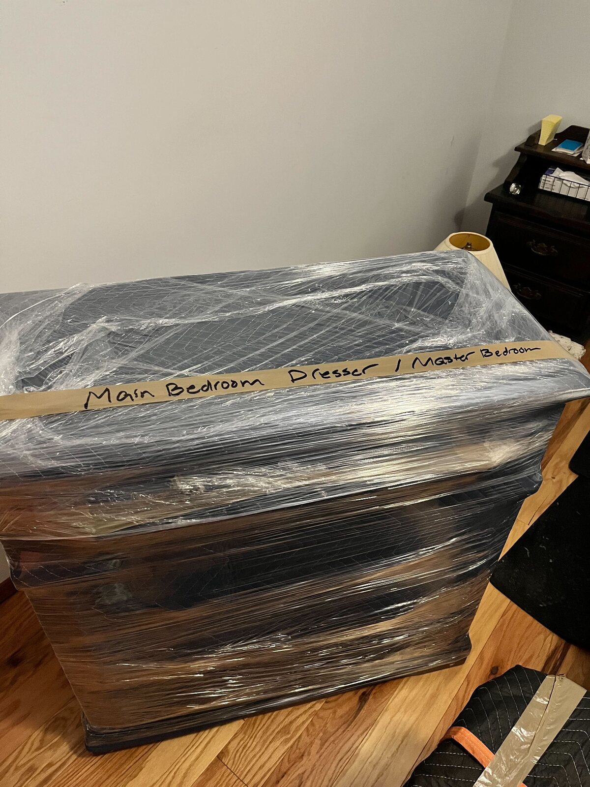 Dresser protected with a moving pad and stretch wrap and labeled for the main bedroom