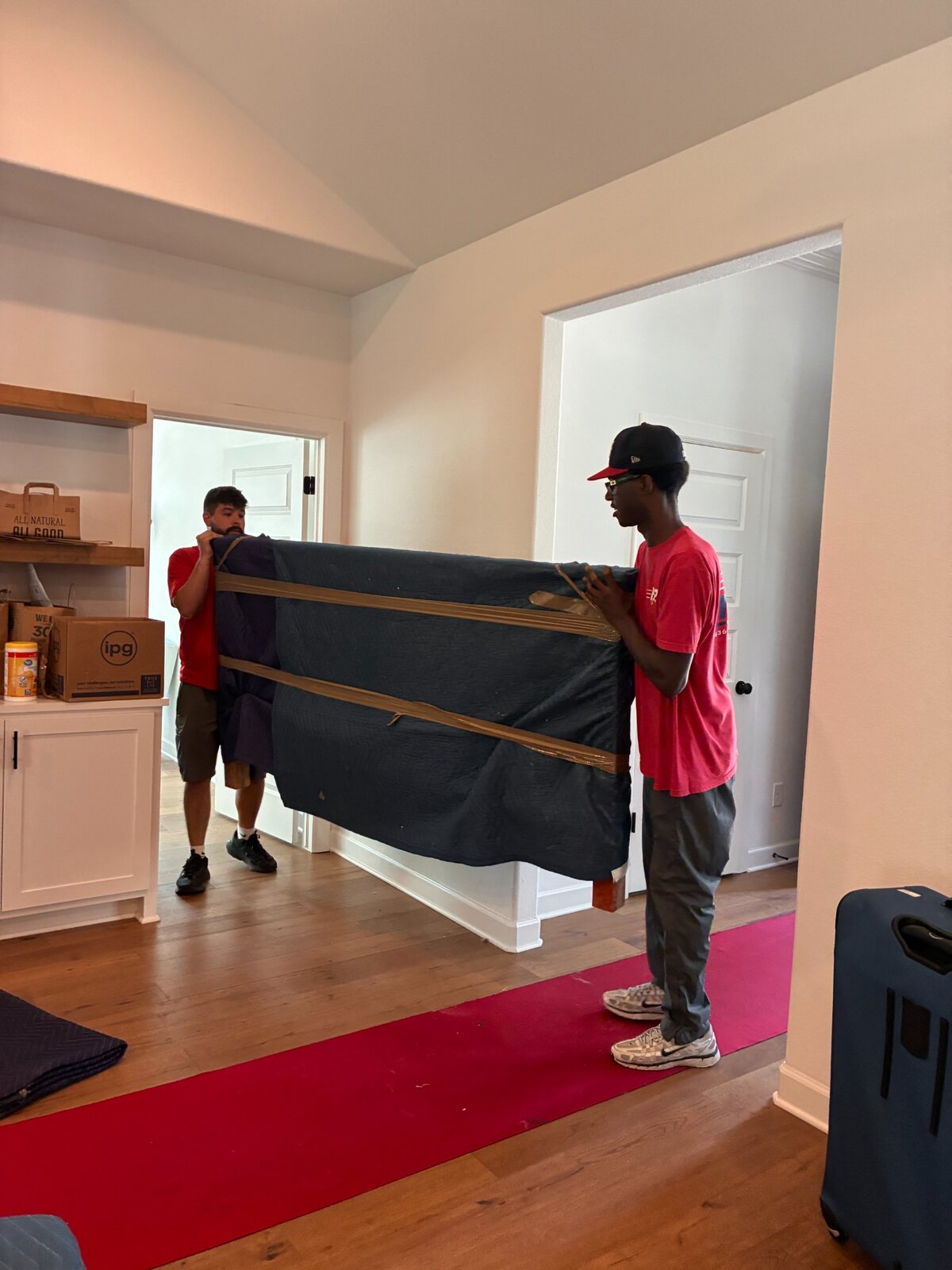 B2 movers Kevin and Hunter carrying a padded footboard inside a Rogers home